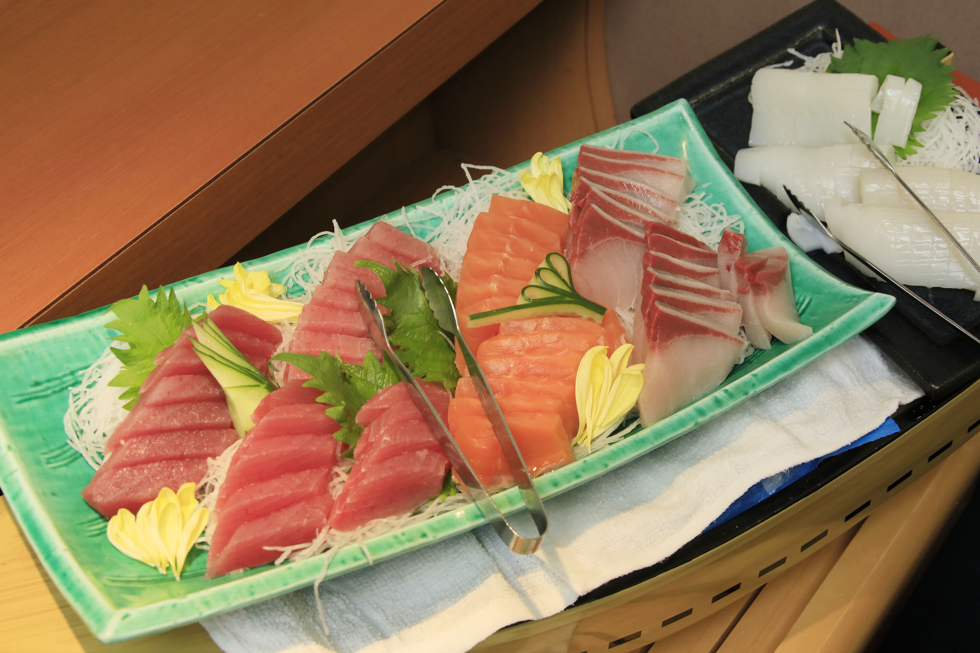 A variety of sashimi on a green plate with a white cloth underneath, placed on a wooden surface.