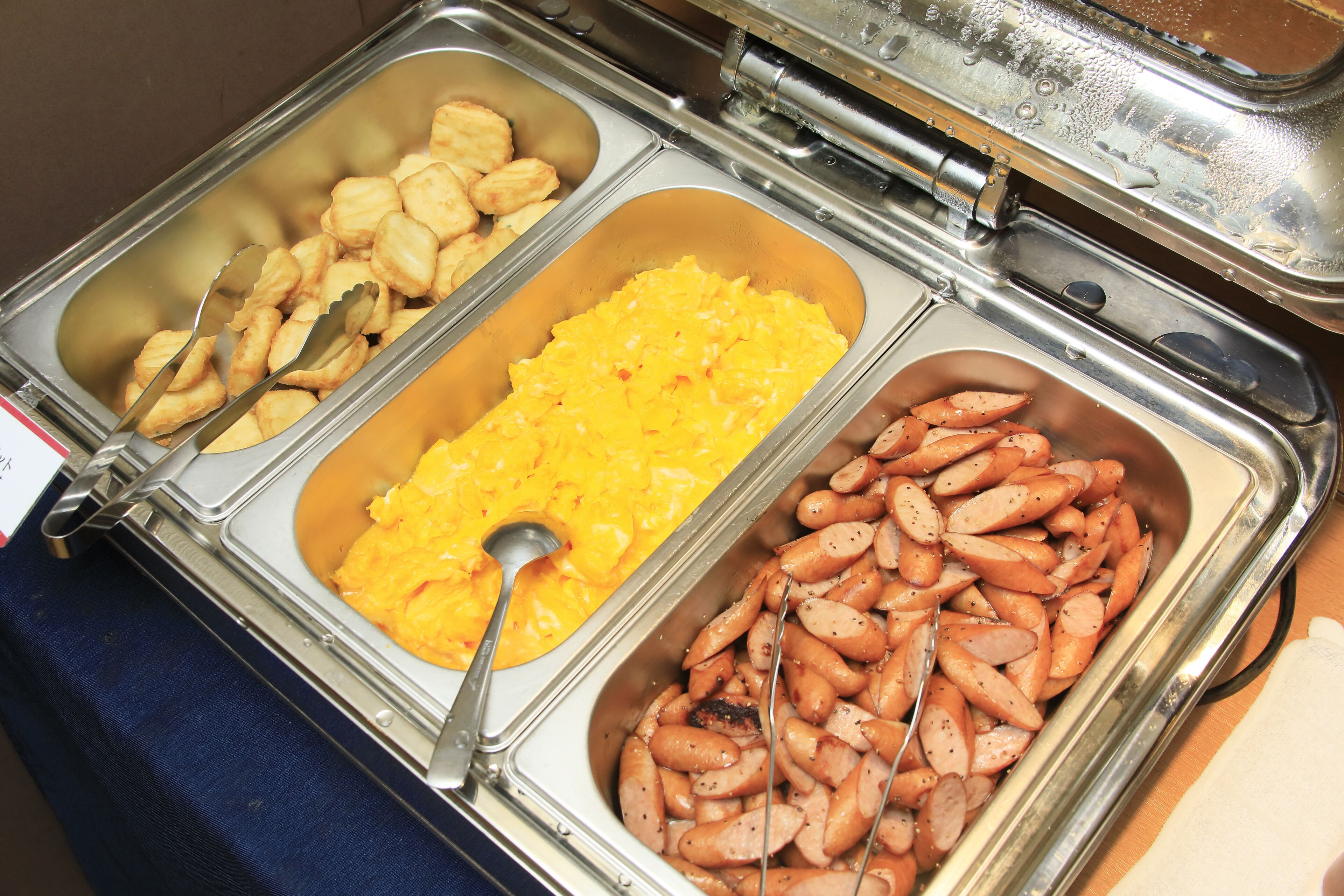Un bufé con tres secciones de comida: un recipiente con galletas, un untable amarillo y una bandeja de salchichas.