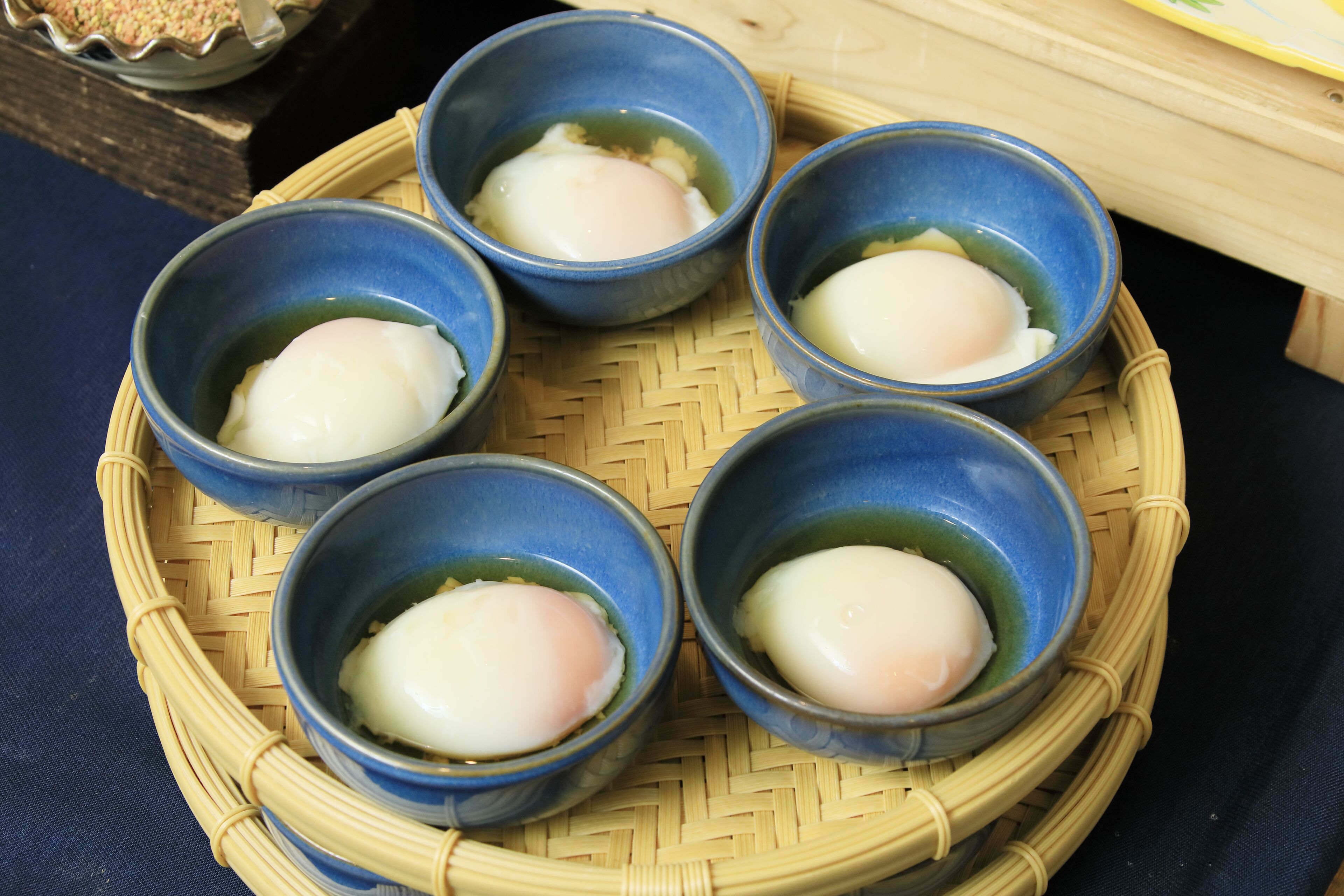 Five blue bowls containing a white, translucent food item on a woven tray.