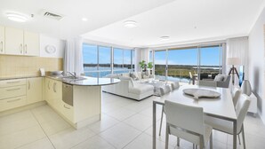 A modern kitchen with a dining area, large windows, and a view of the outdoors. - The Duporth Riverside (Maroochydore)