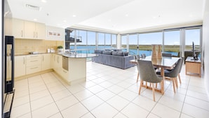A modern kitchen with a dining area, large windows, and a view of the sea. - The Duporth Riverside (Maroochydore)