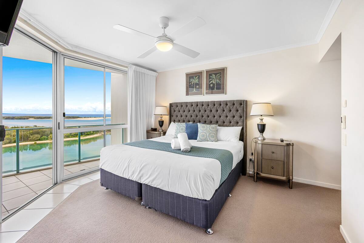 A bedroom with a large bed, a ceiling fan, and a view of the beach.