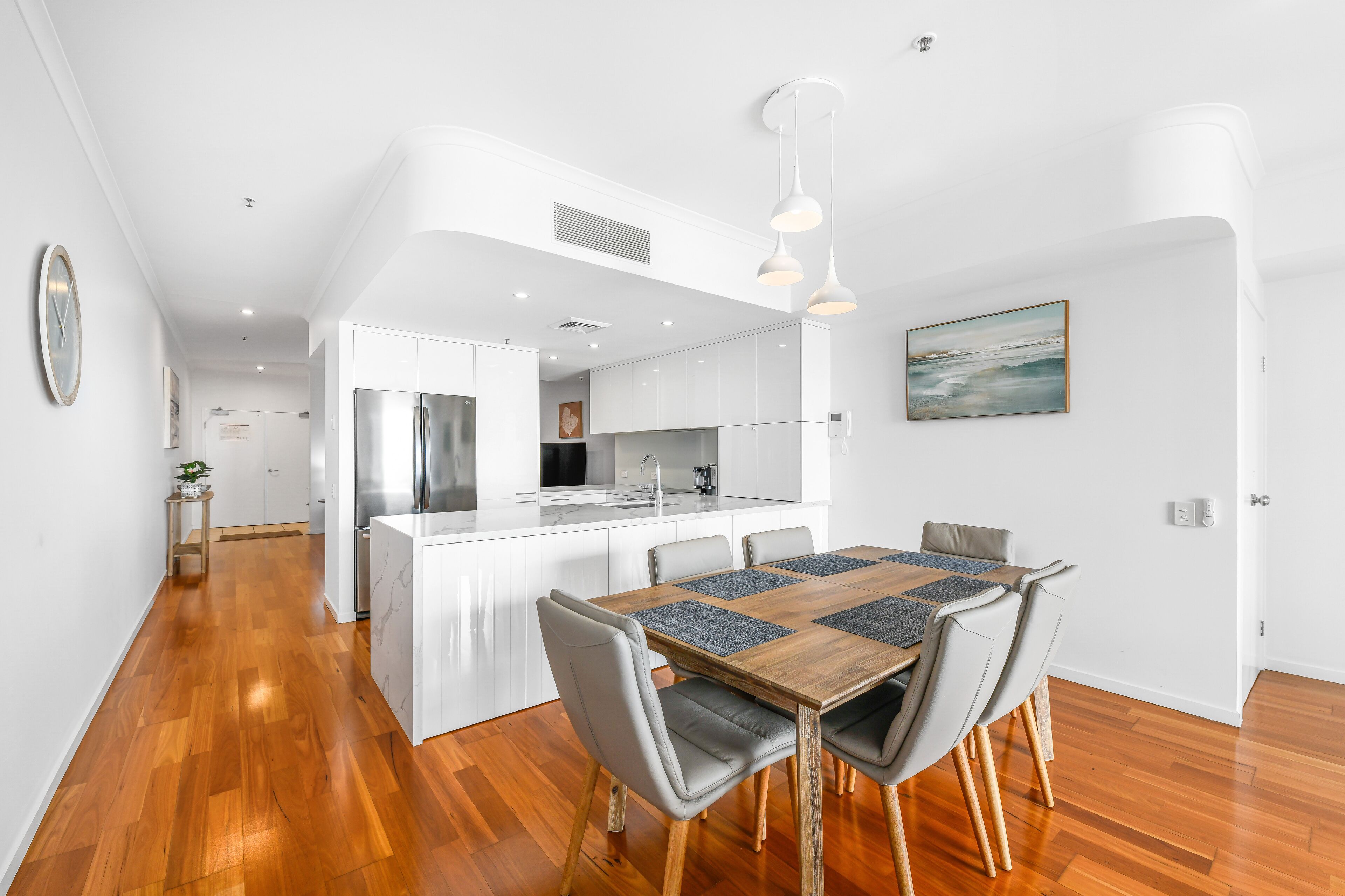 A modern kitchen with white cabinetry, a central island, and a dining area with a wooden table and chairs.
