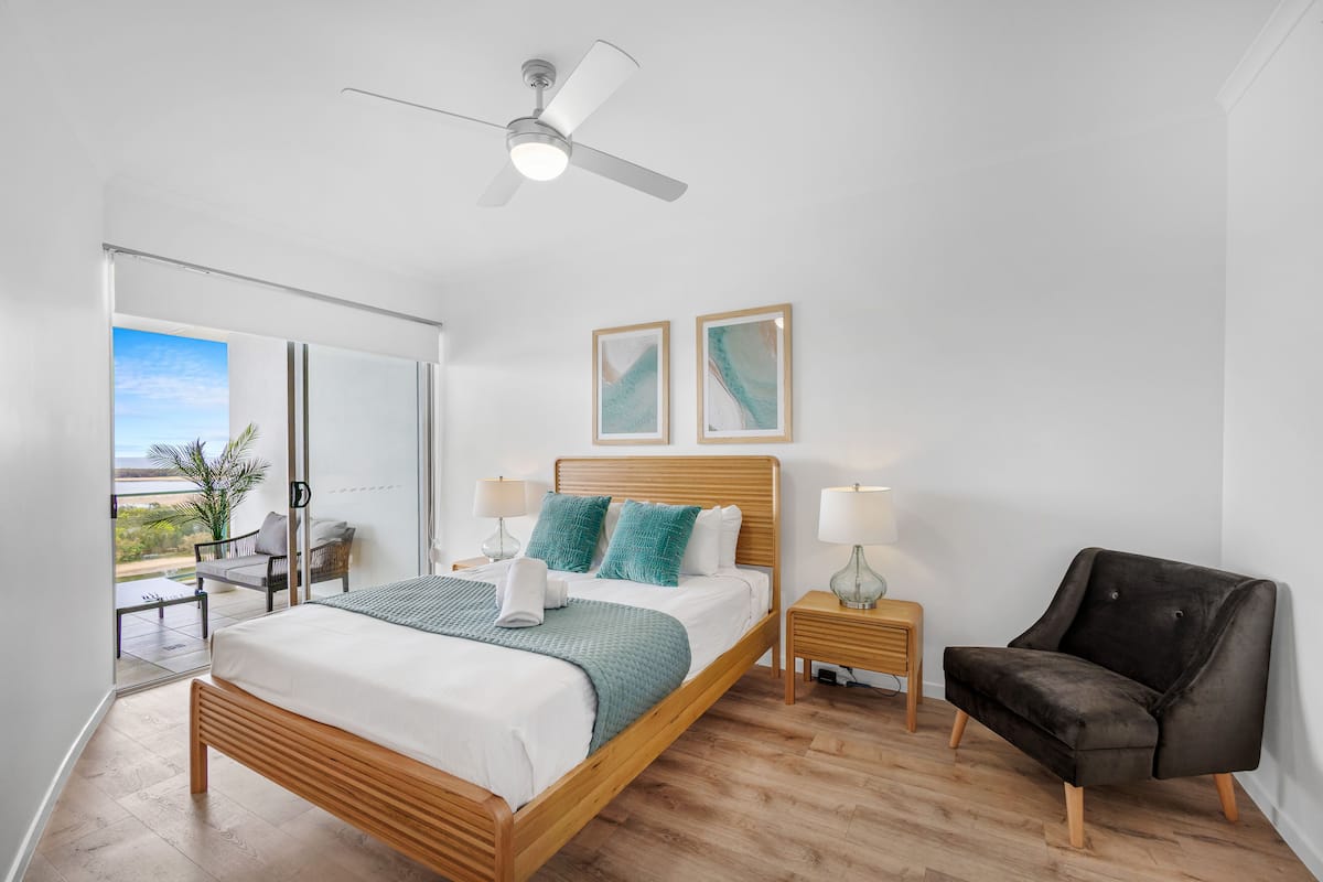 A modern bedroom with a wooden bed, bedside lamps, a ceiling fan, and two framed artworks on the wall.