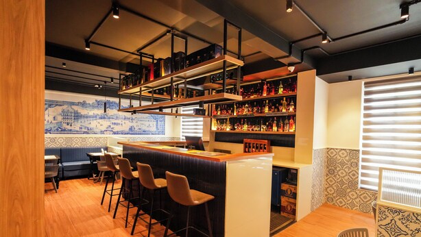 Una zona de bar con mostrador, taburetes y estantes llenos de botellas.