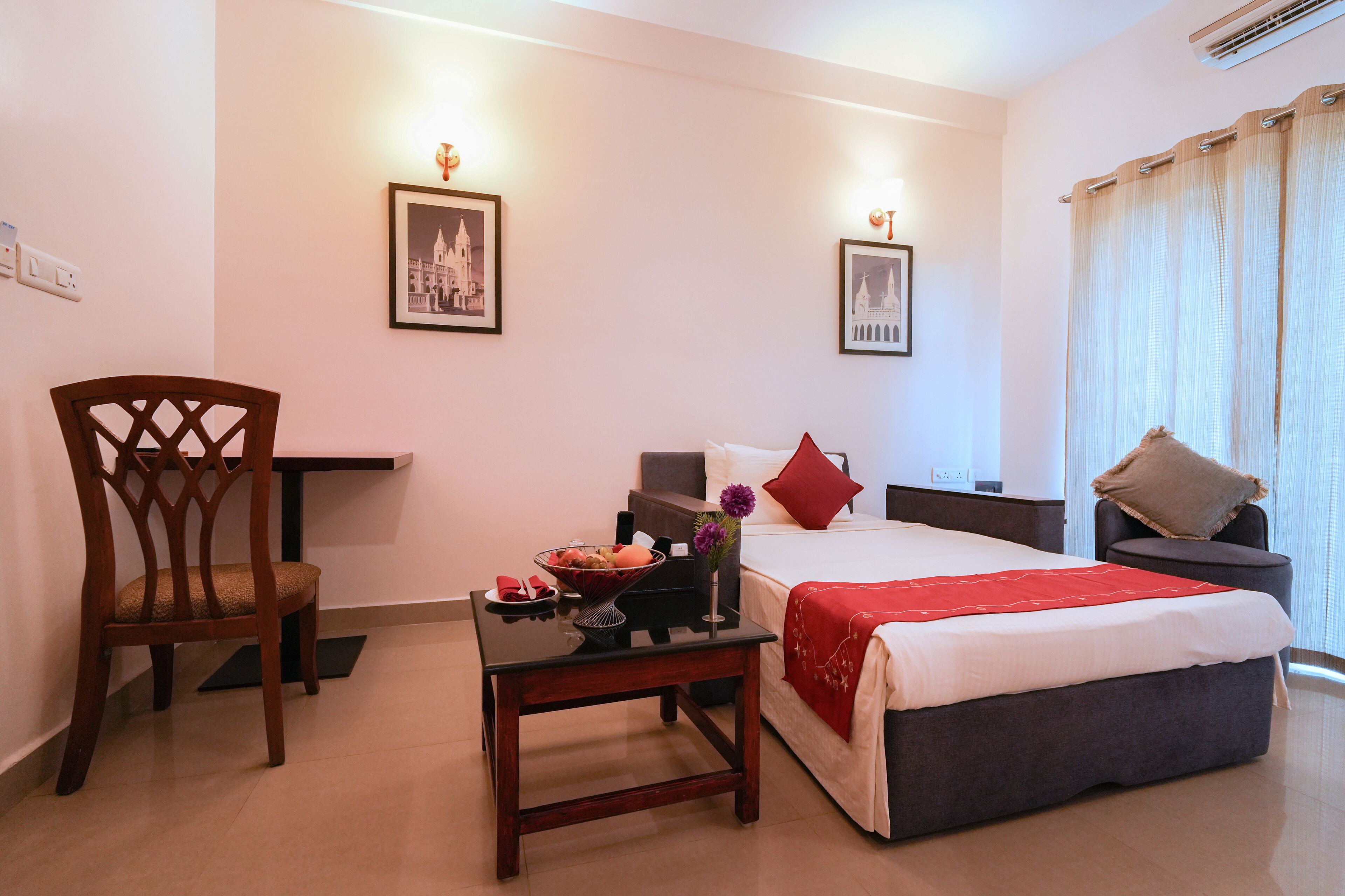 A hotel room with a bed, a desk, a chair, and two framed pictures on the wall.