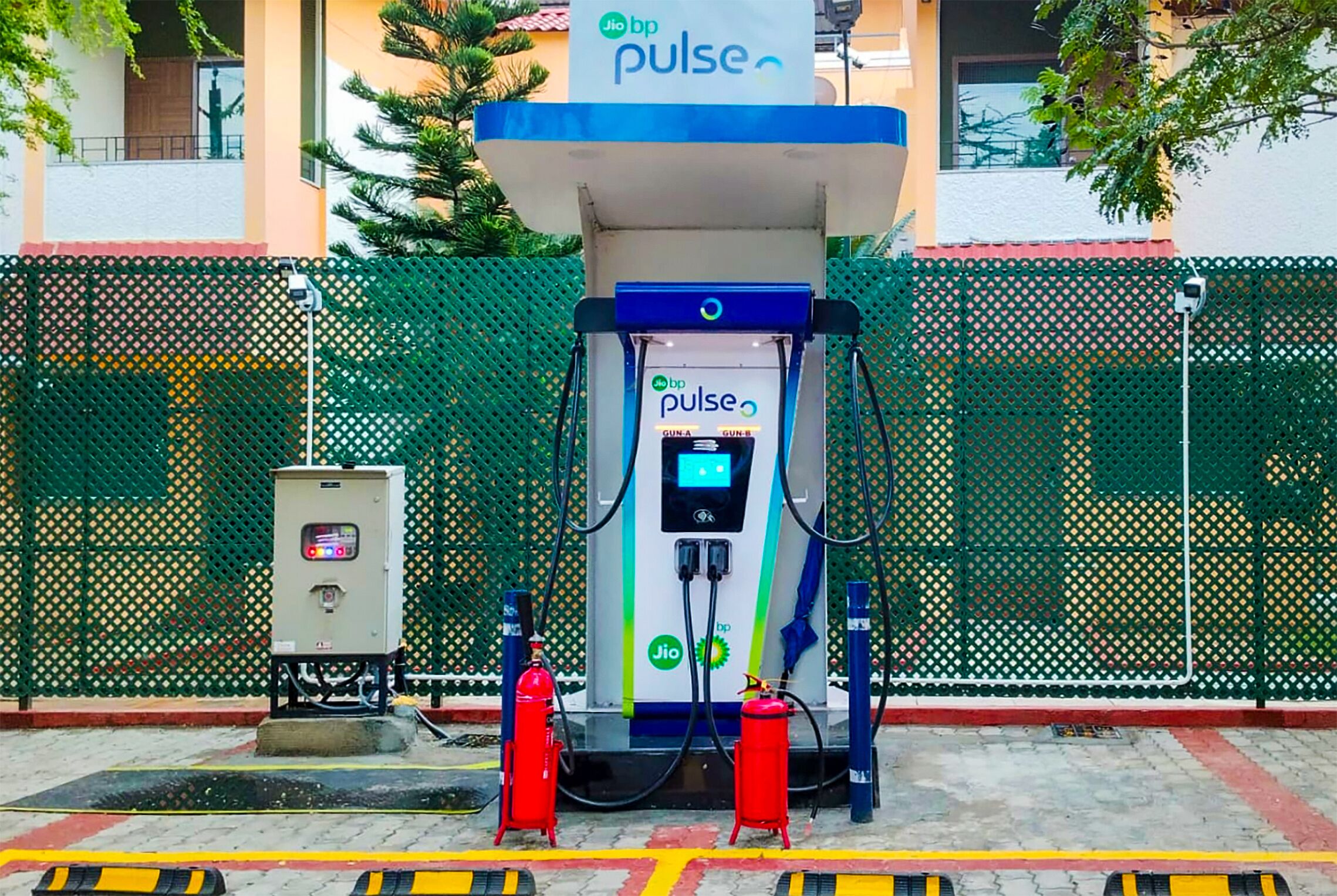 A Jio BP Pulse electric vehicle charging station with two red fire extinguishers and a utility box.