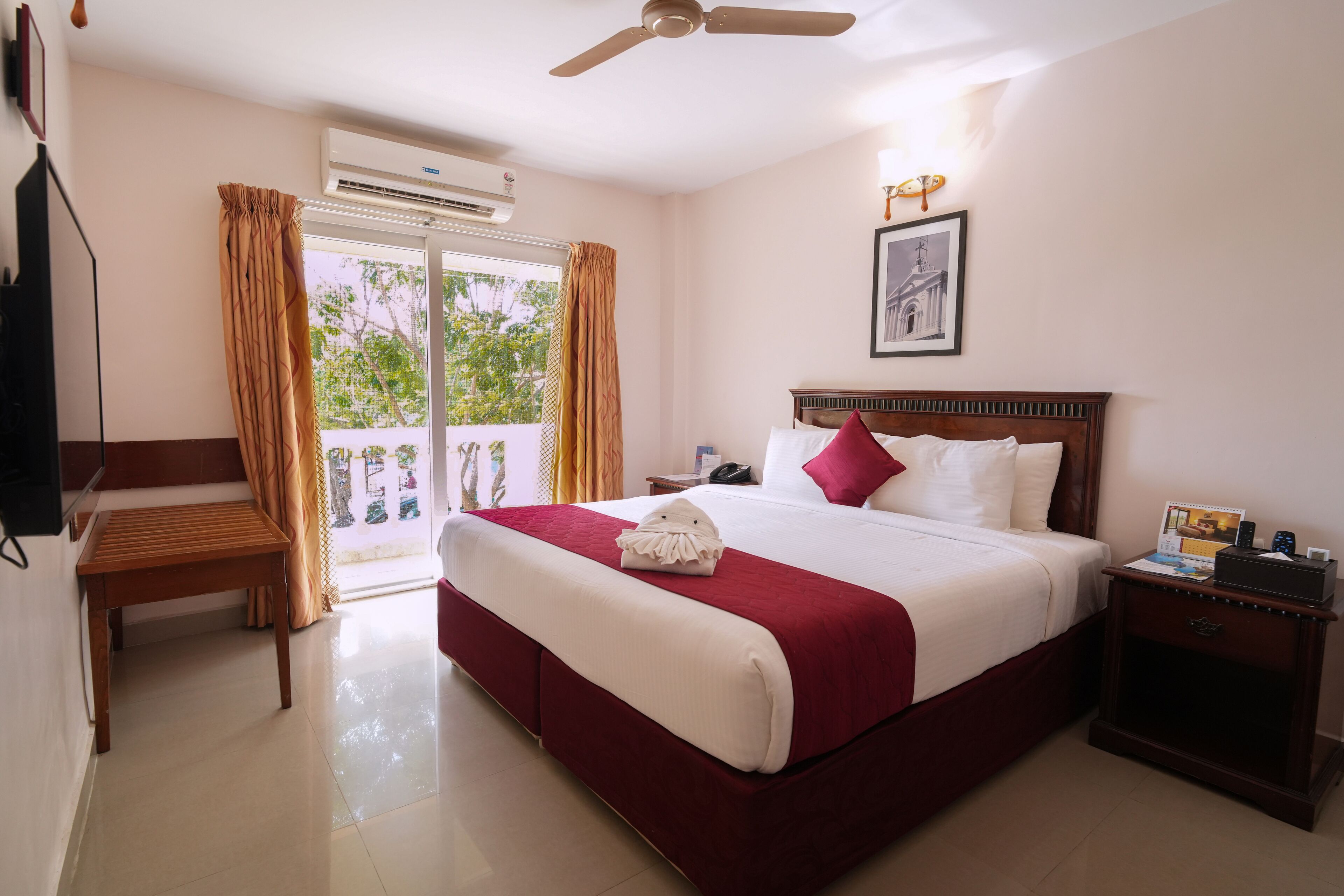 A hotel room with a large bed, a wooden nightstand, a desk, and a ceiling fan.