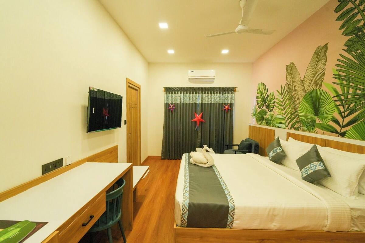 Ein Hotelzimmer mit Bett, Schreibtisch, Stuhl, Fernseher und Deckenventilator.