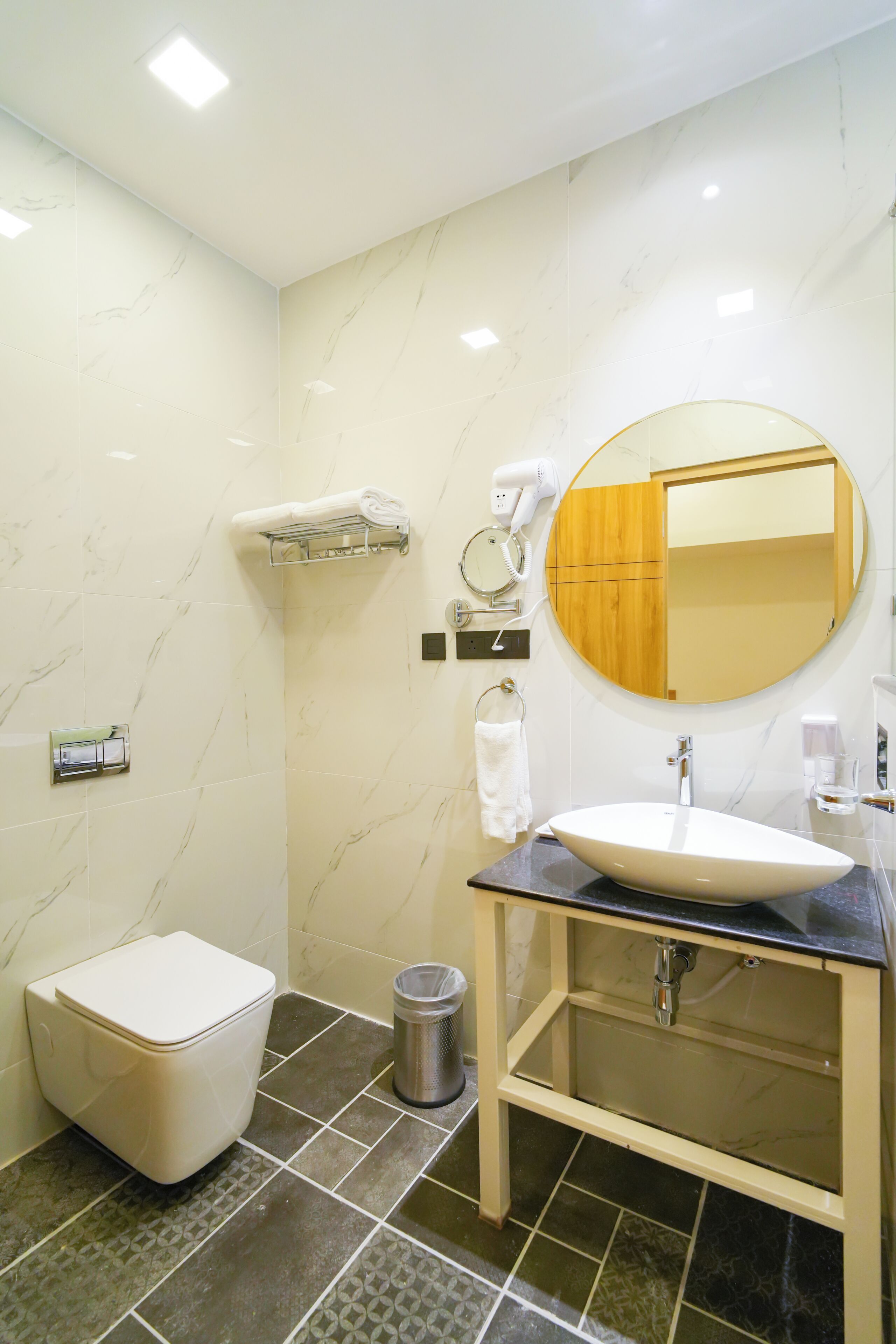 Egy modern fürdőszoba, amelyben található egy WC, mosdókagyló, tükör, törölközőtartó és hajszárító.