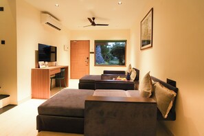 A modern living room with a flat-screen TV, a ceiling fan, and a large window with a view of greenery.