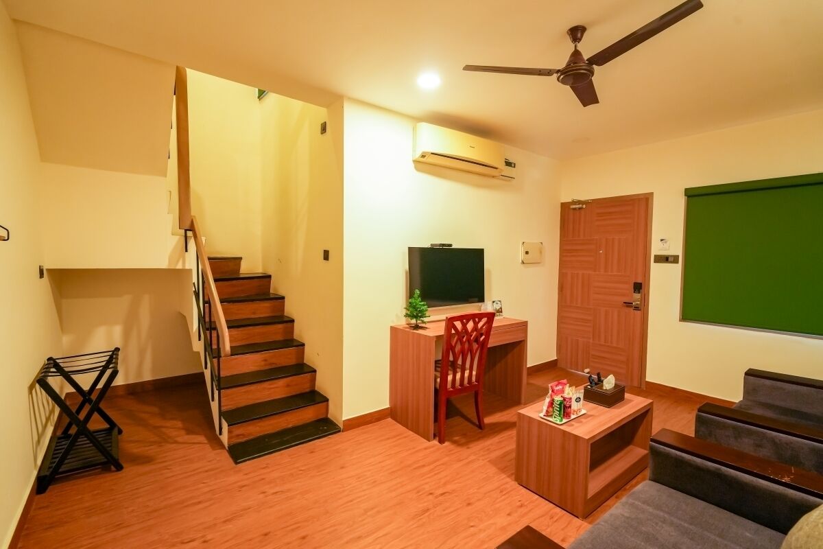 A living room with a staircase, a desk with a chair, a television, and a green screen wall.