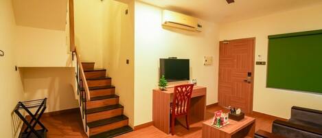 A living room with a staircase, a desk with a chair, a television, and a green screen wall.