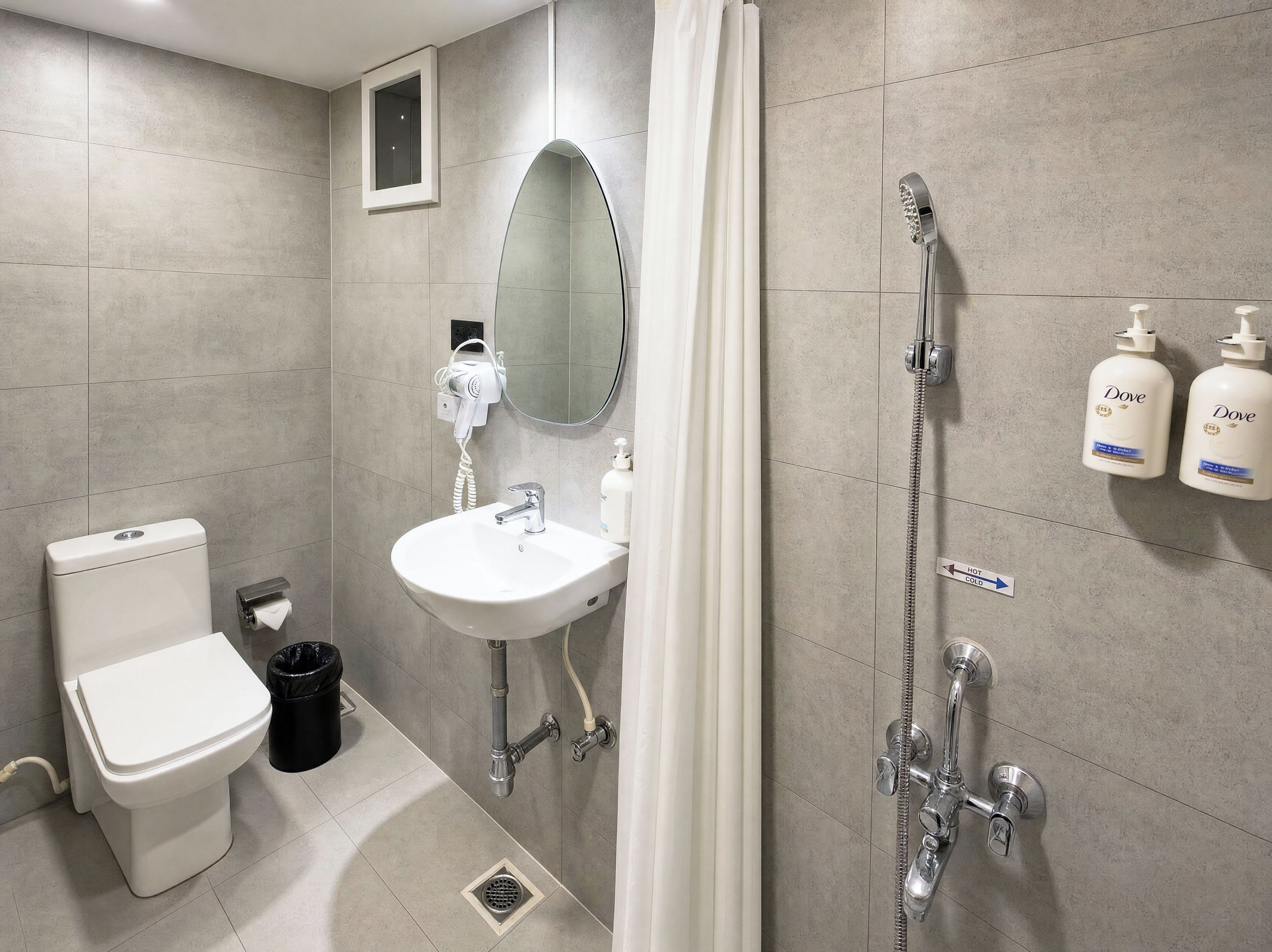A modern bathroom with a toilet, sink, shower, and two Dove hand soap bottles.