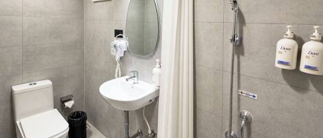 A modern bathroom with a toilet, sink, shower, and two Dove hand soap bottles.