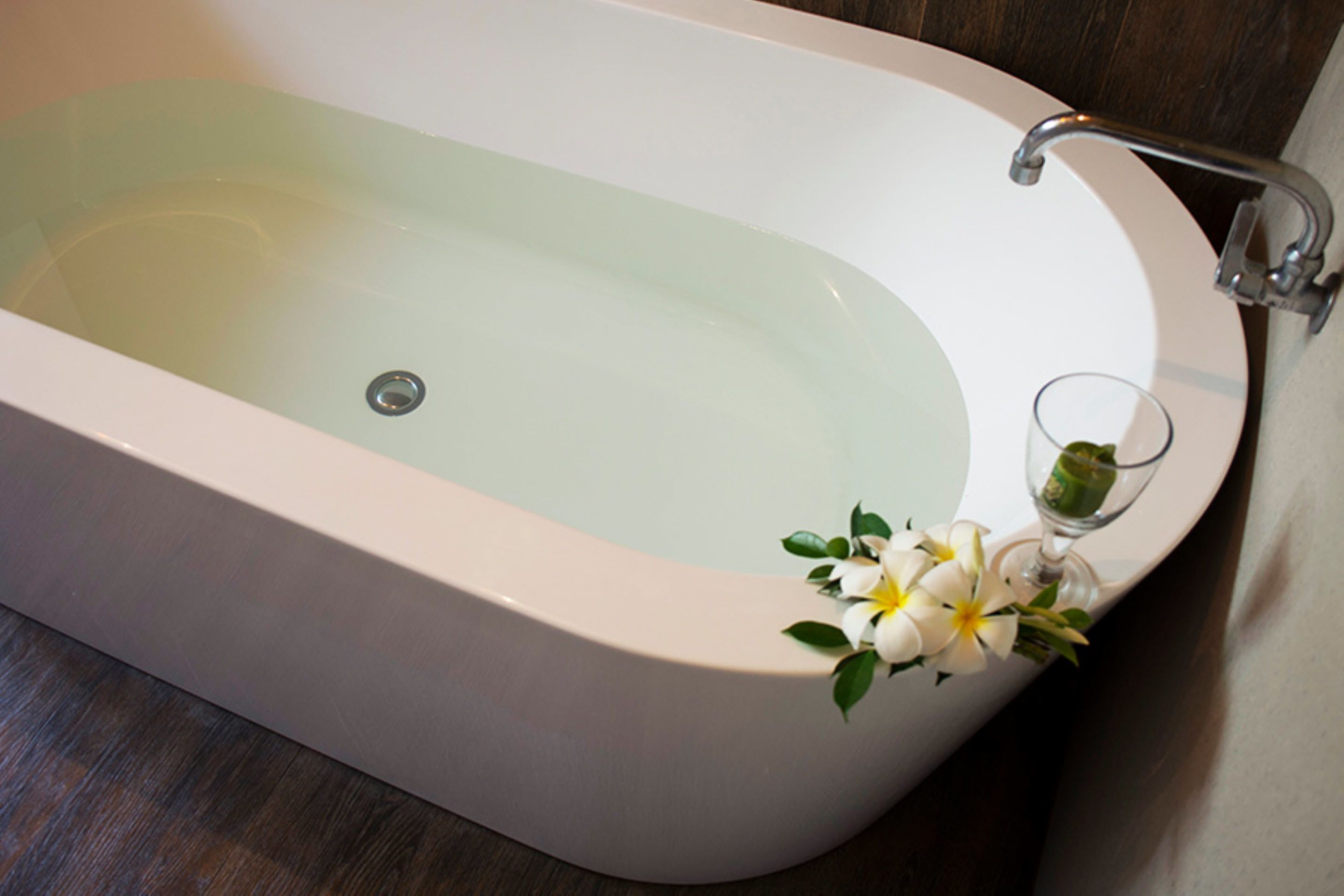 A bathtub with a glass of water and a flower arrangement.