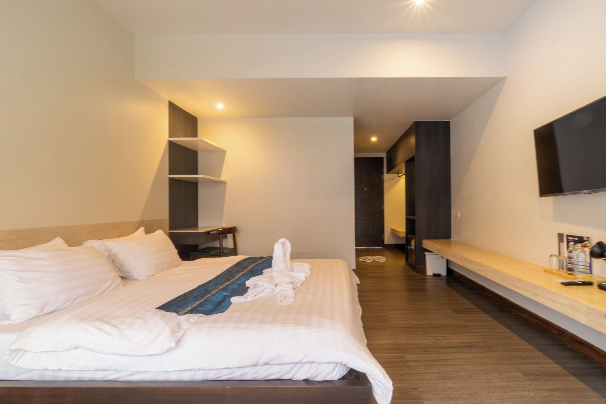 A hotel room with a bed, bedside table, TV, and a bench along the wall.