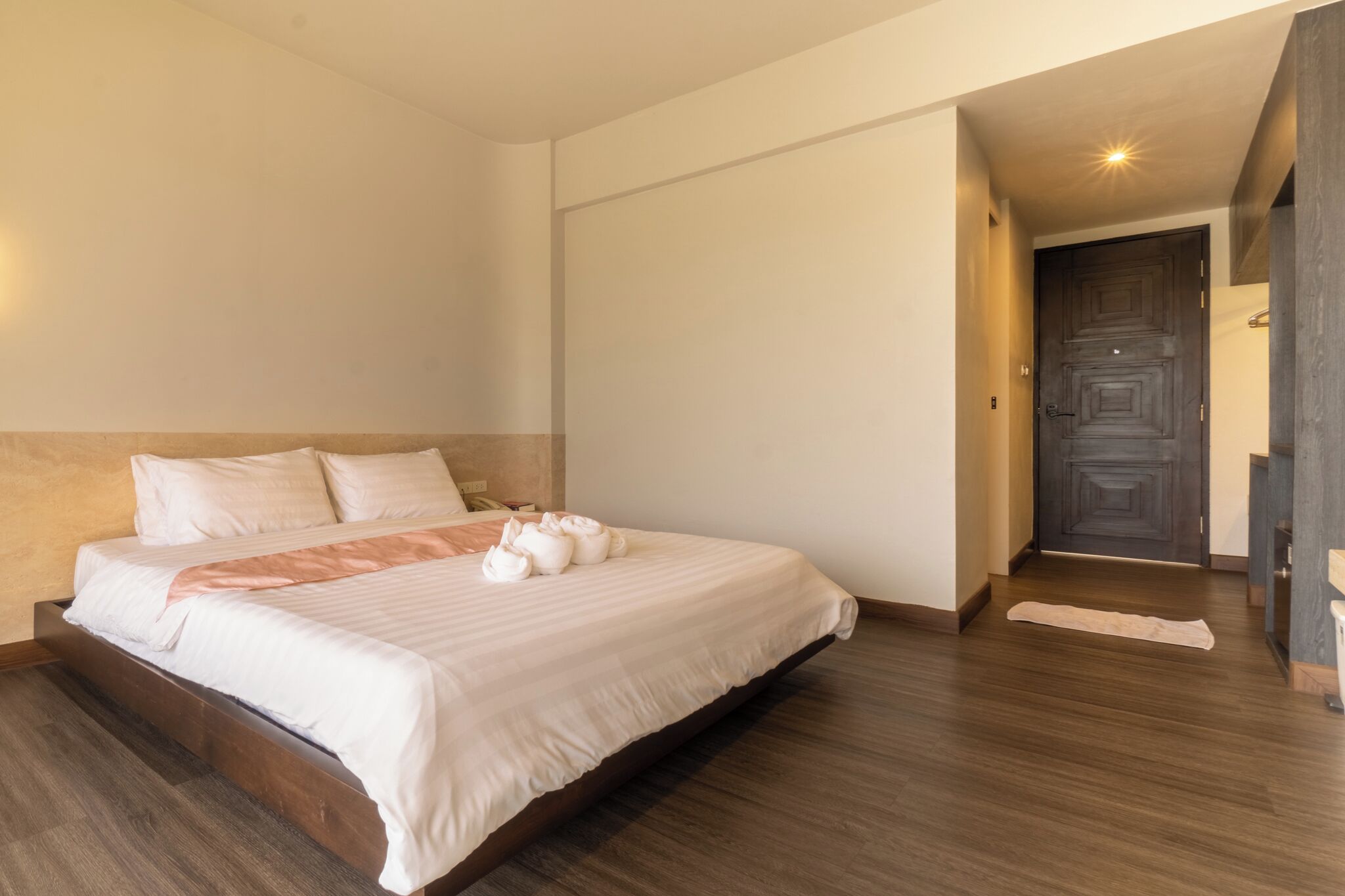 A hotel room with a large bed, a wooden headboard, a dark wooden door, and a small rug on the floor.