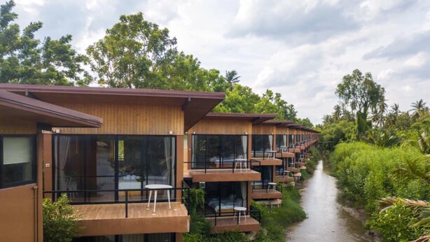 Una hilera de bungalows modernos de madera con balcones de vidrio que dan a un río, rodeados de exuberante vegetación.
