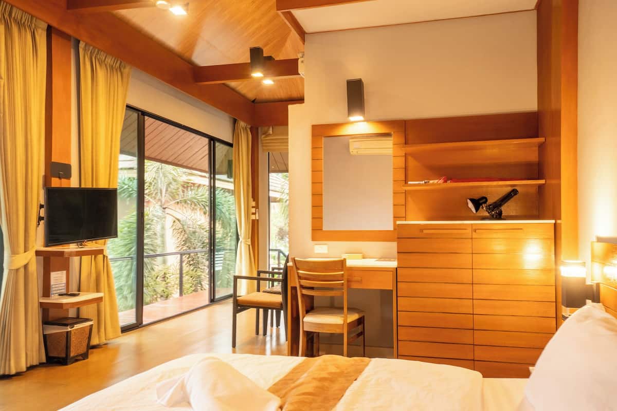 Une chambre à coucher comprenant un lit, un bureau, une chaise, un téléviseur et une grande fenêtre avec des rideaux.