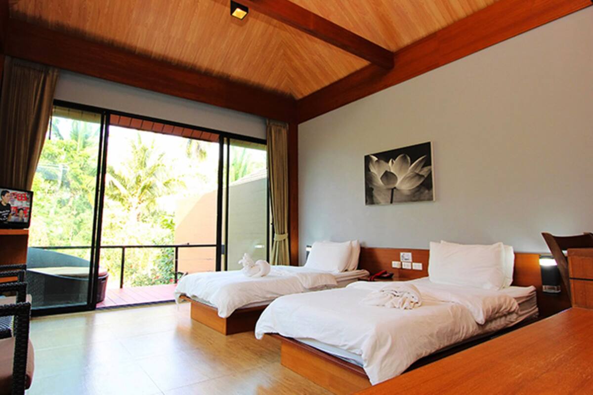 Une chambre d’hôtel avec deux lits, un plafond en bois, une grande fenêtre donnant sur un paysage verdoyant et un tableau encadré au mur.