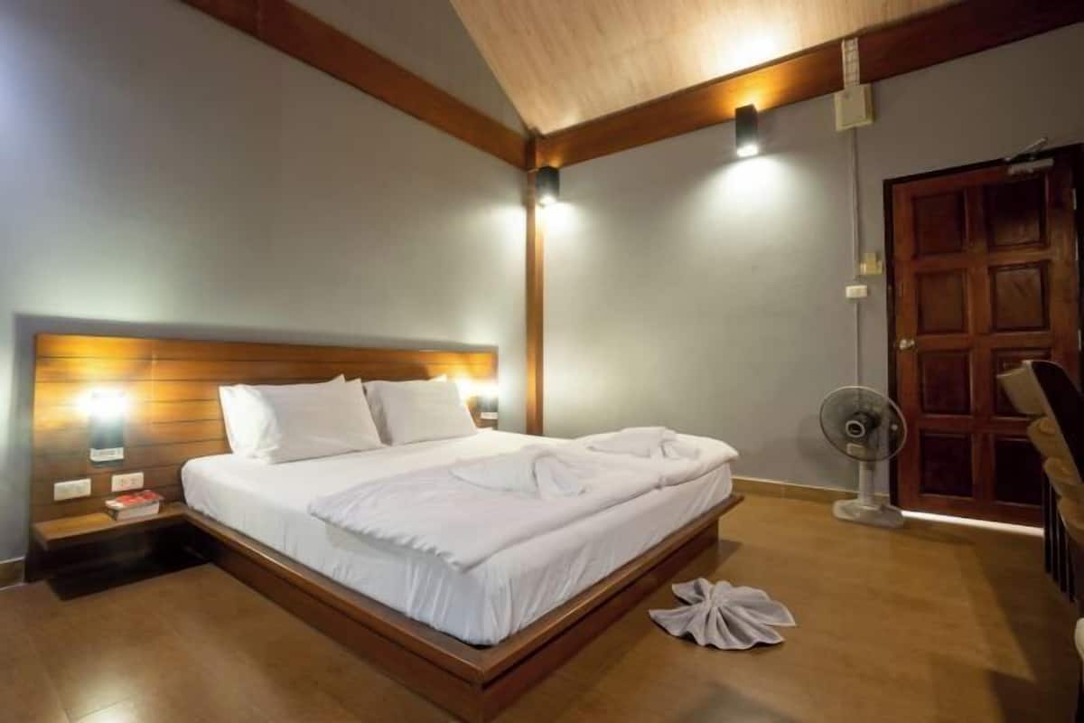 Un lit bien fait, avec du linge de lit blanc, une tête de lit en bois, des lampes de chevet et un ventilateur sur pied.