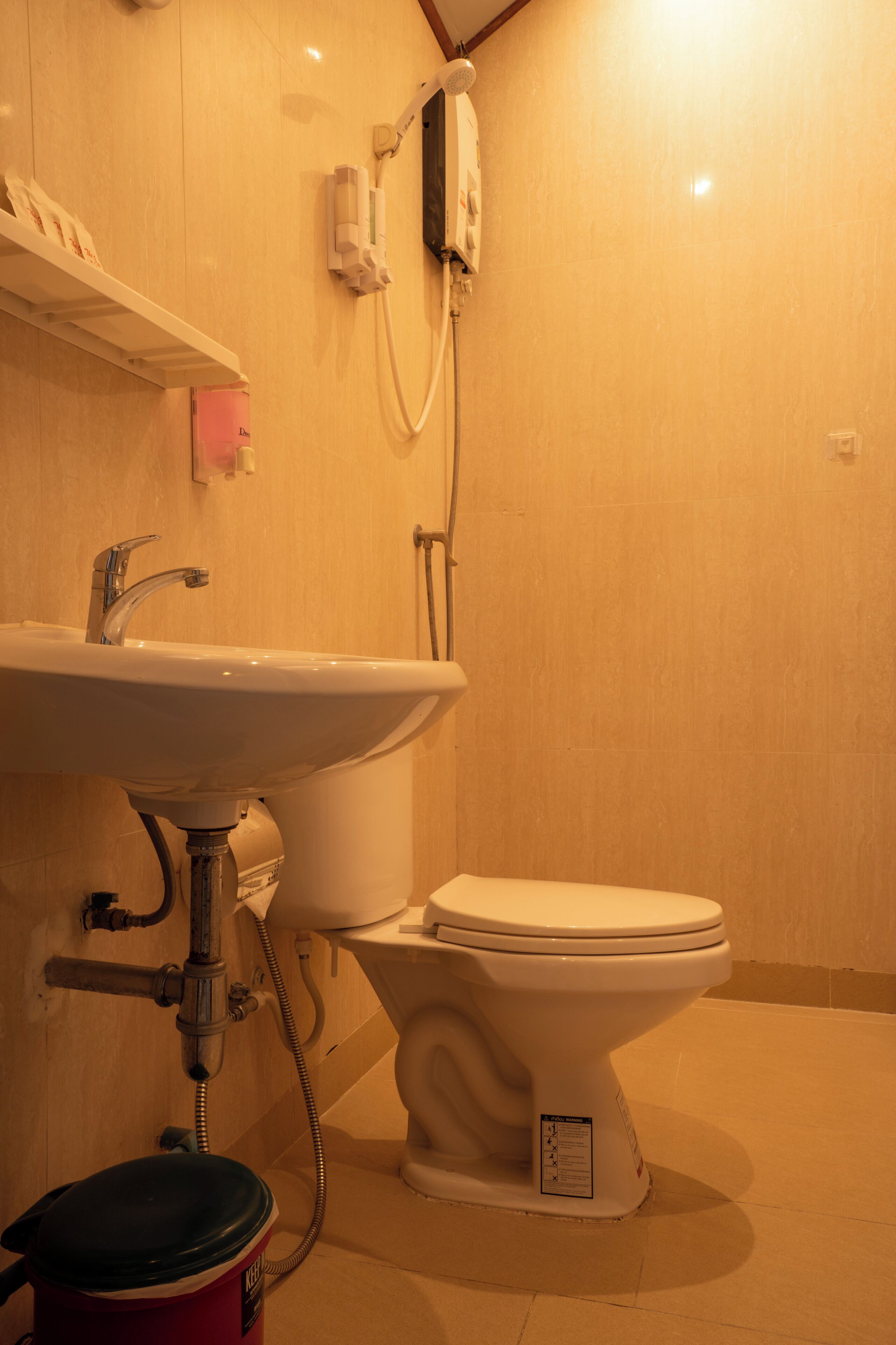Un baño con lavamanos, inodoro y cabezal de ducha en la pared.