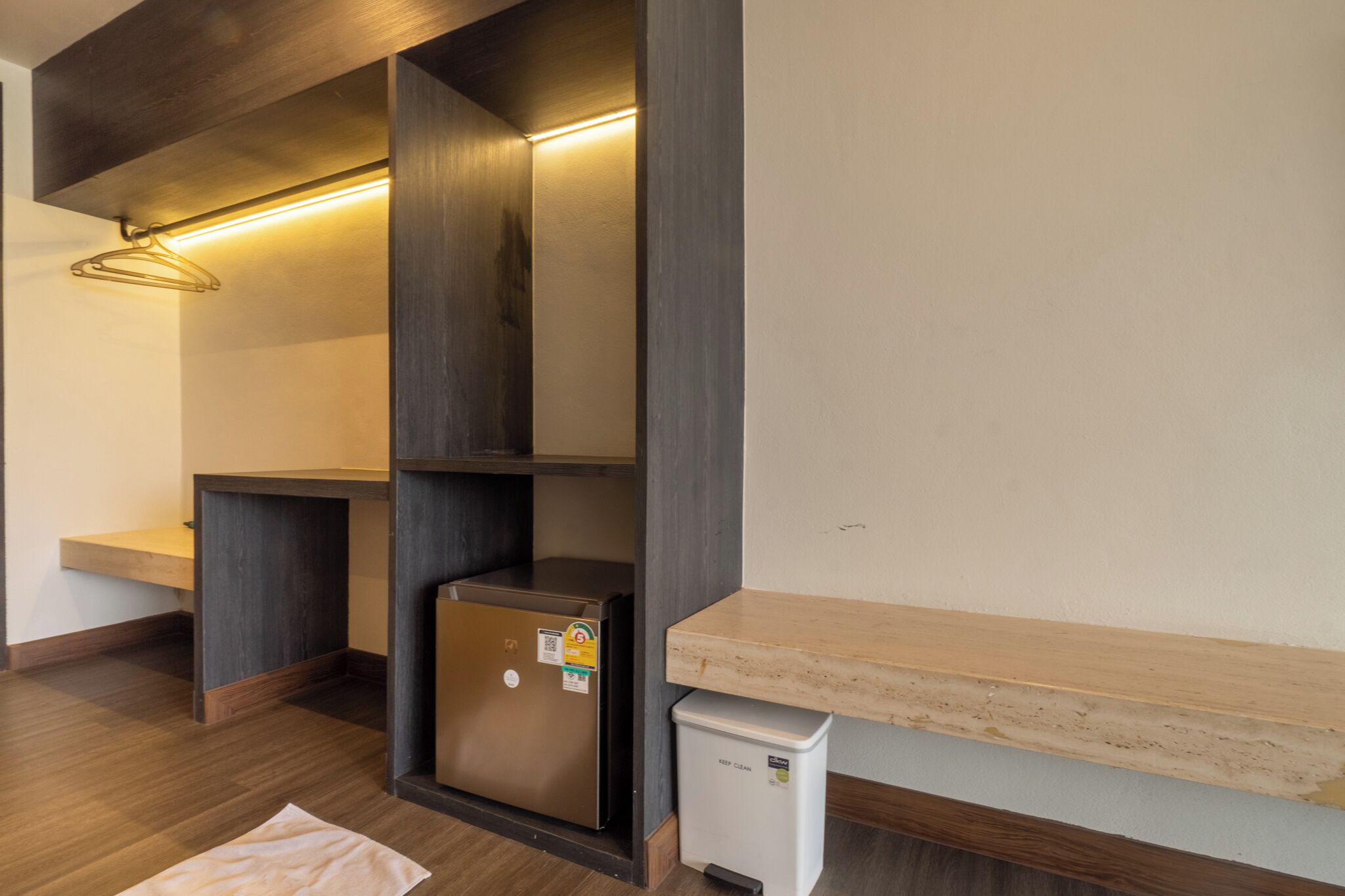 A modern room with built-in wooden shelves, a small refrigerator, and a bench.