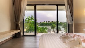 Habitación de hotel con una cama grande, un banco y vistas a una playa y palmeras.