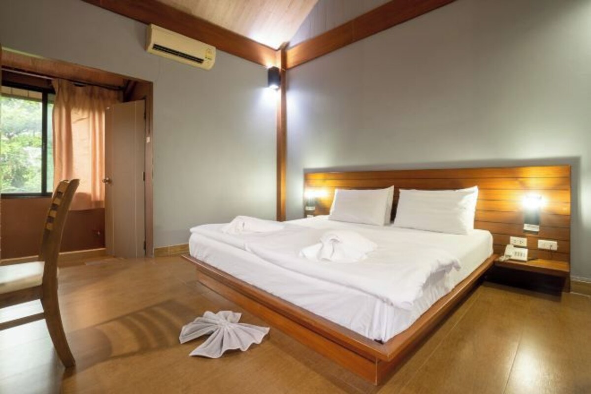 A neatly made bed with white linens and a wooden headboard, a wooden chair, and a bedside table with a lamp.