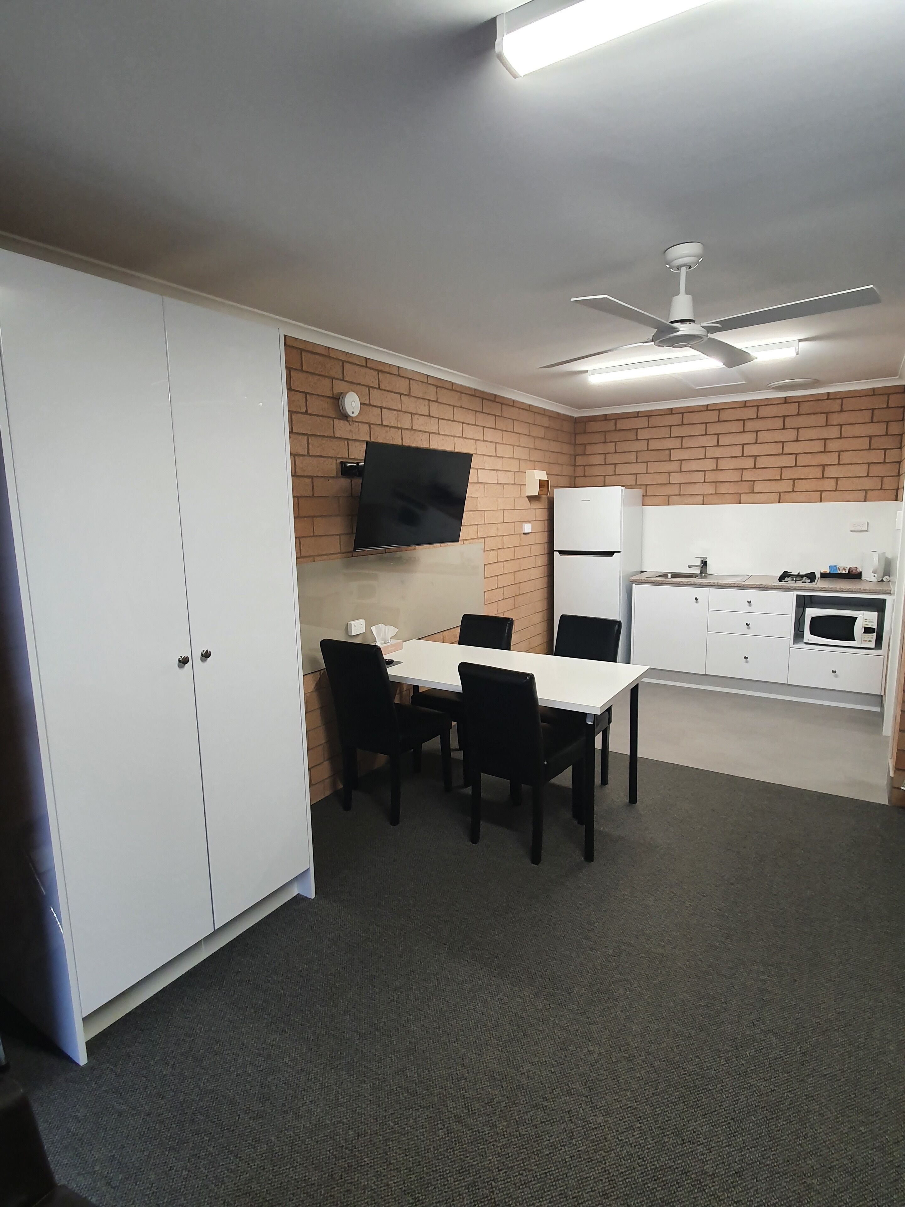 A compact kitchen with a dining area, white cabinets, a flat-screen TV, and a ceiling fan.