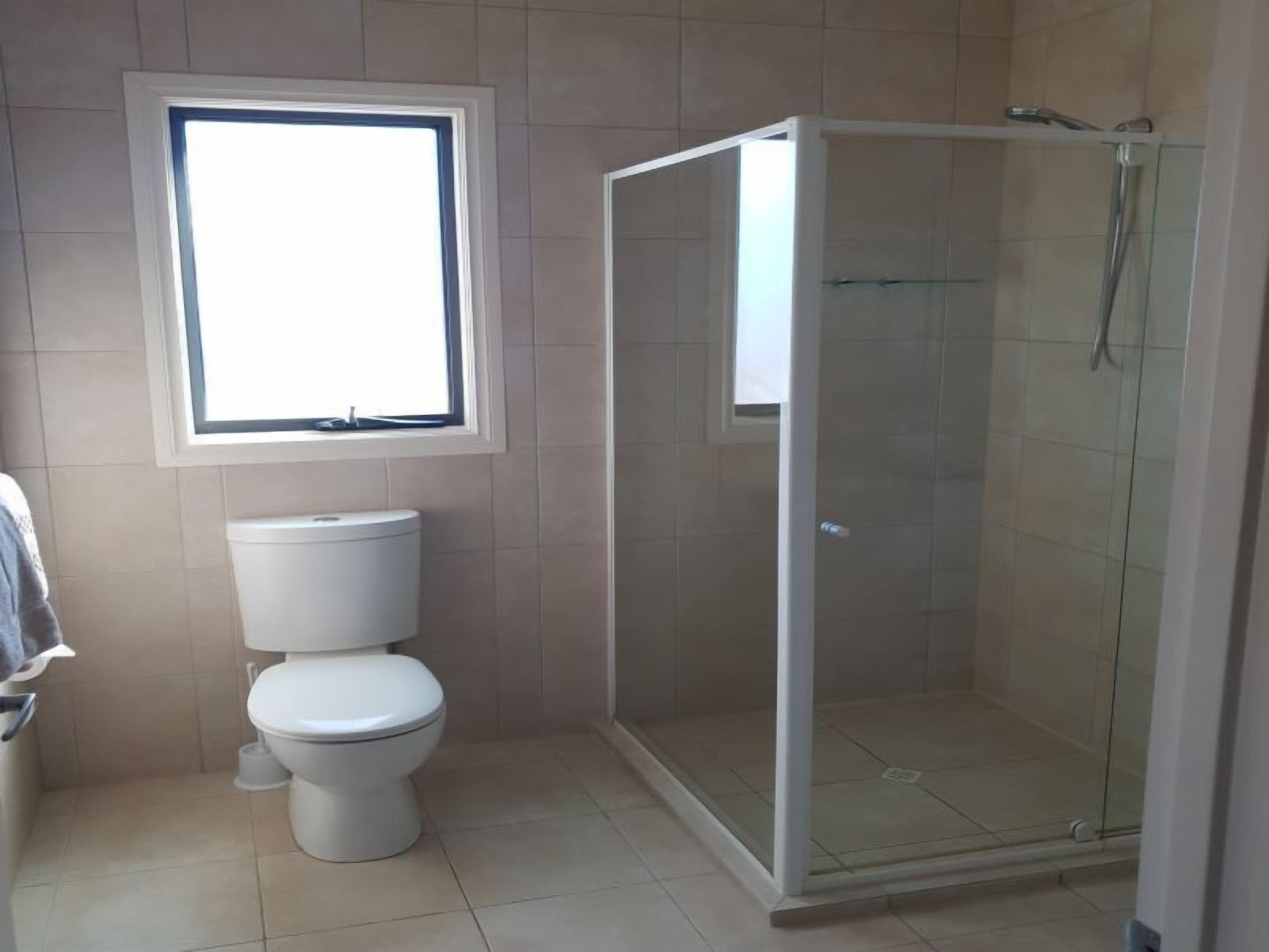 Een badkamer met toilet, raam en douche met glazen wanden.