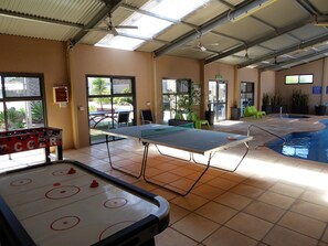 Un espace de loisirs intérieur comprenant une table de baby-foot, une table de ping-pong et une table de billard.