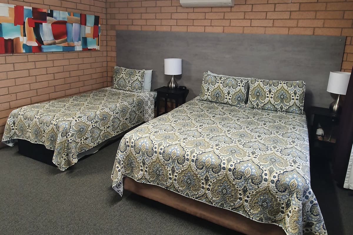 A hotel room with two beds, a brick wall, a colorful abstract painting, and an air conditioning unit.