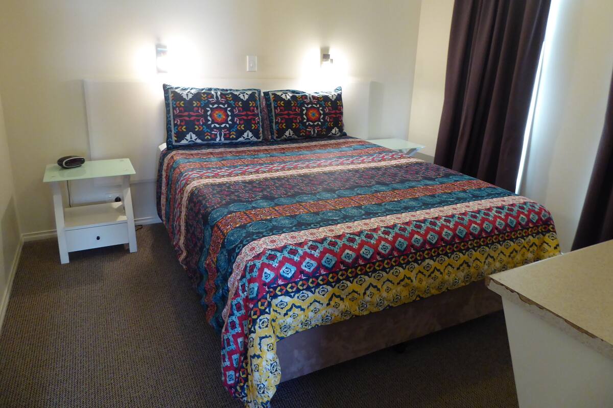 A bedroom with a bed, a nightstand, a lamp, and a window with curtains.
