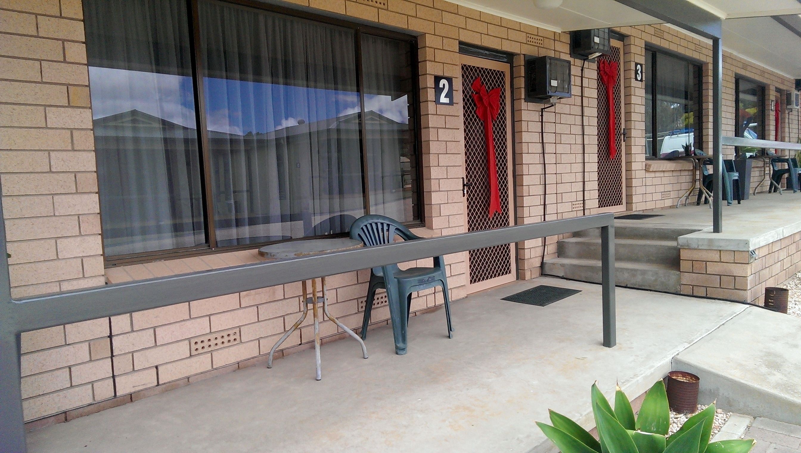 Un bâtiment à la façade en briques, avec une salle numérotée 2, un espace extérieur abrité avec une table et des chaises, et une petite marche menant à l’entrée.