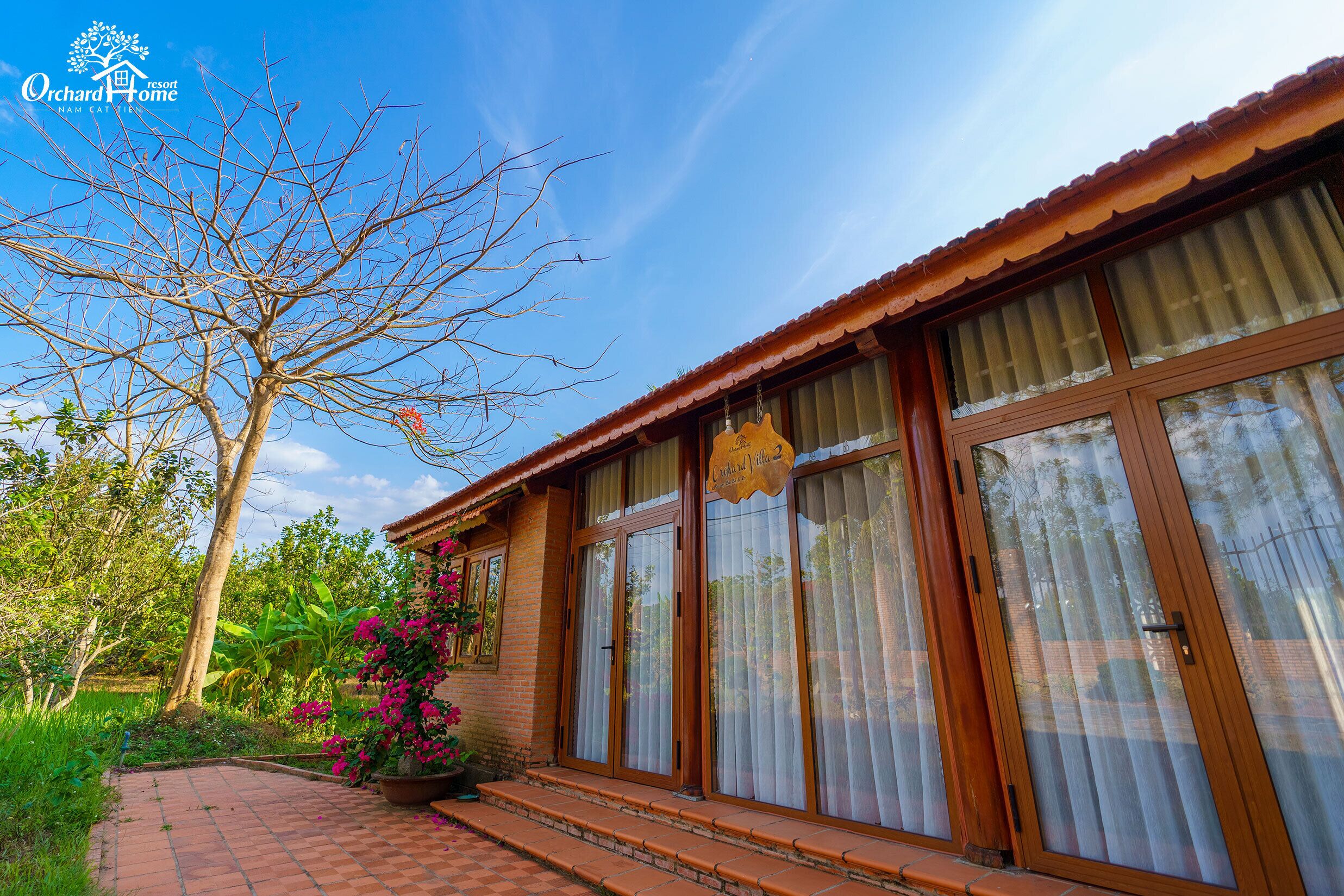 A resort-style building with large windows, a brick pathway, and lush greenery.