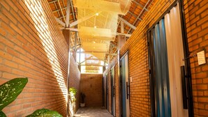 A narrow corridor with brick walls, potted plants, and doors leading to rooms.