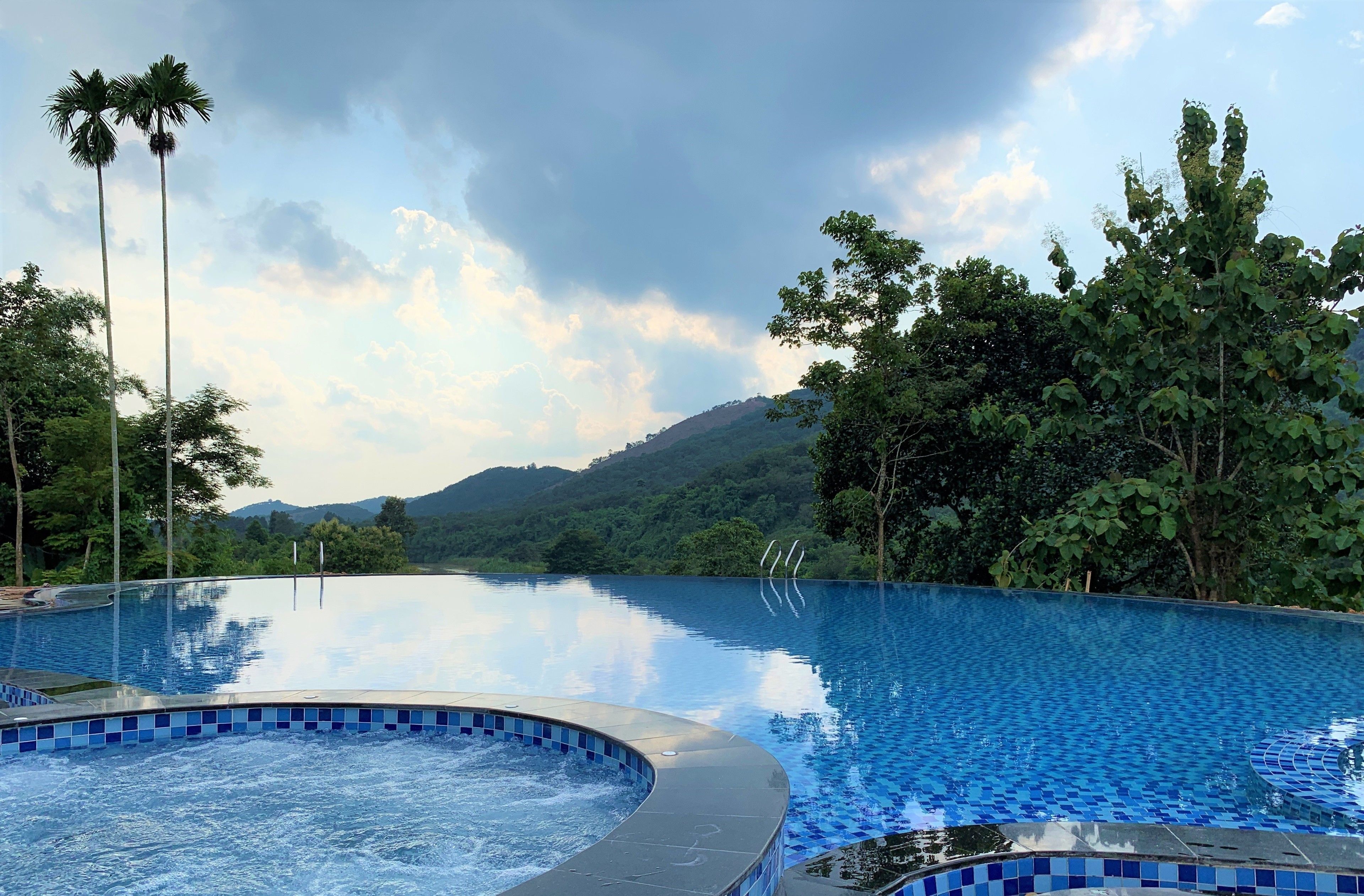 A swimming pool with a hot tub, surrounded by lush greenery and a mountainous backdrop.