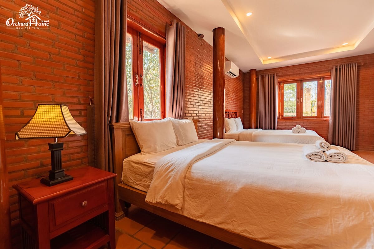 Une chambre d’hôtel avec un mur en briques, deux lits, une table de chevet et une lampe.