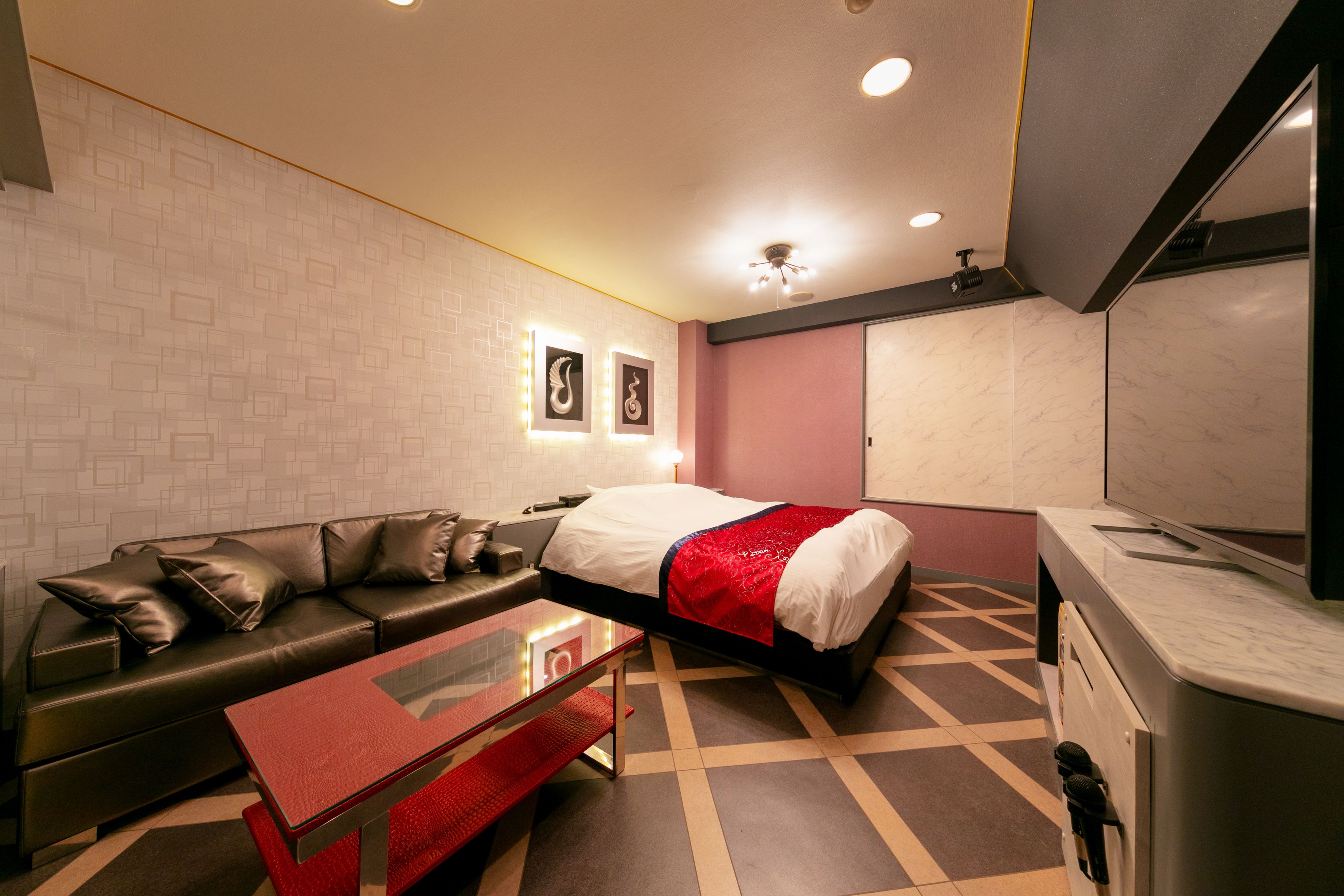 A modern hotel room with a bed, a sofa, a coffee table, and a bathroom with a mirror and cabinet.