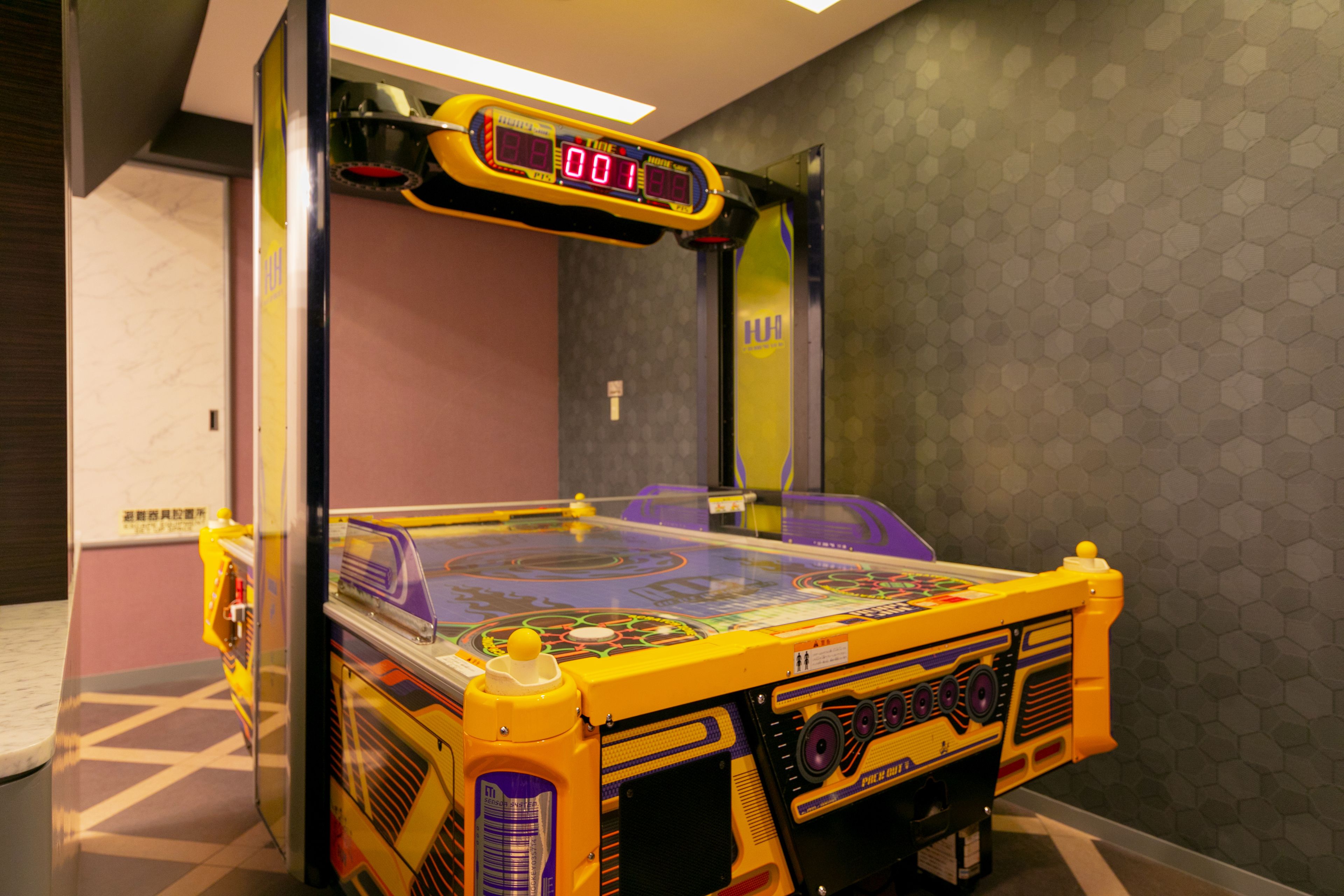 A pinball machine in a room with a hexagonal patterned wall and a door in the background.