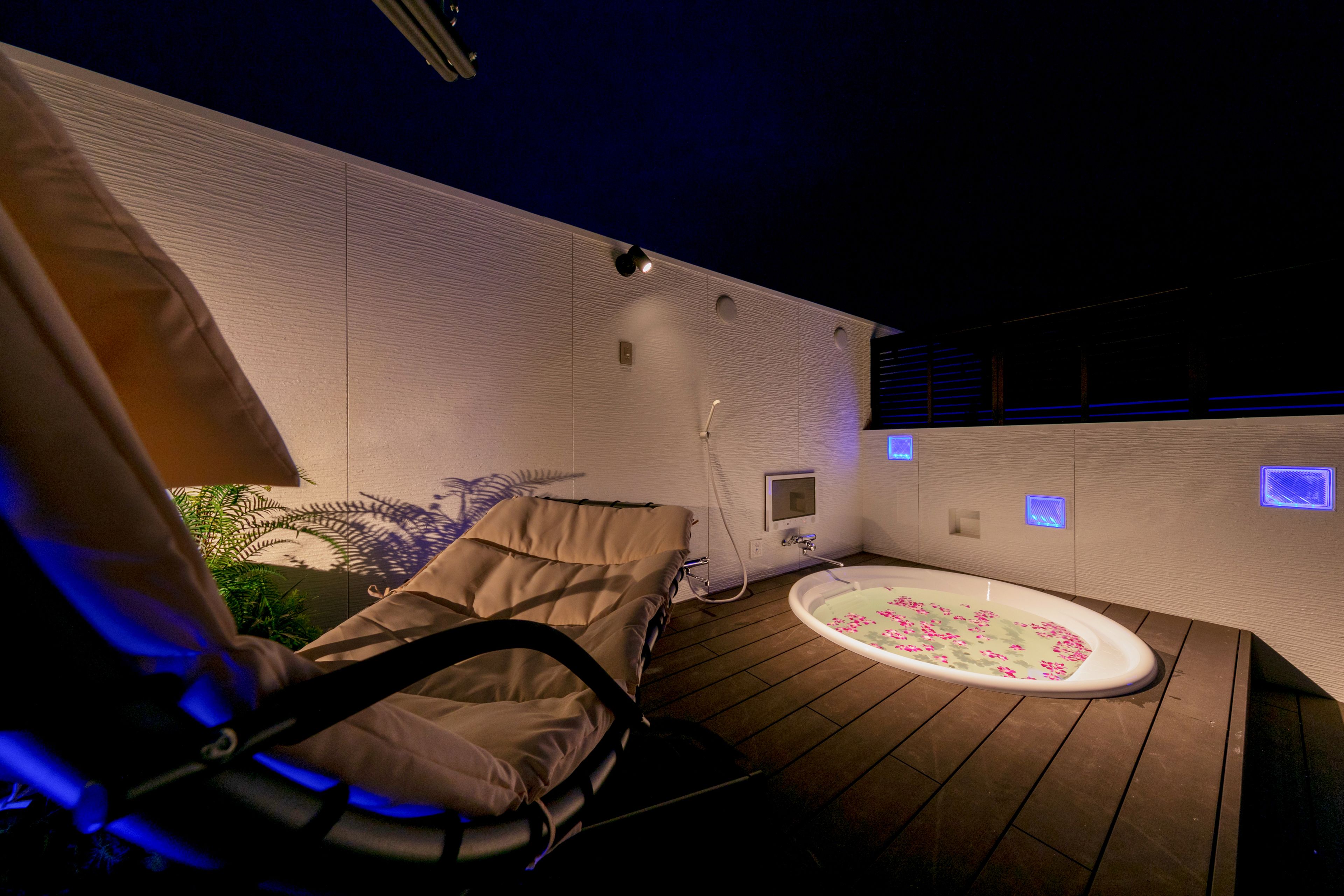A spa room with a massage chair, a small bathtub with floral bath mat, and wall-mounted massage therapy lights.