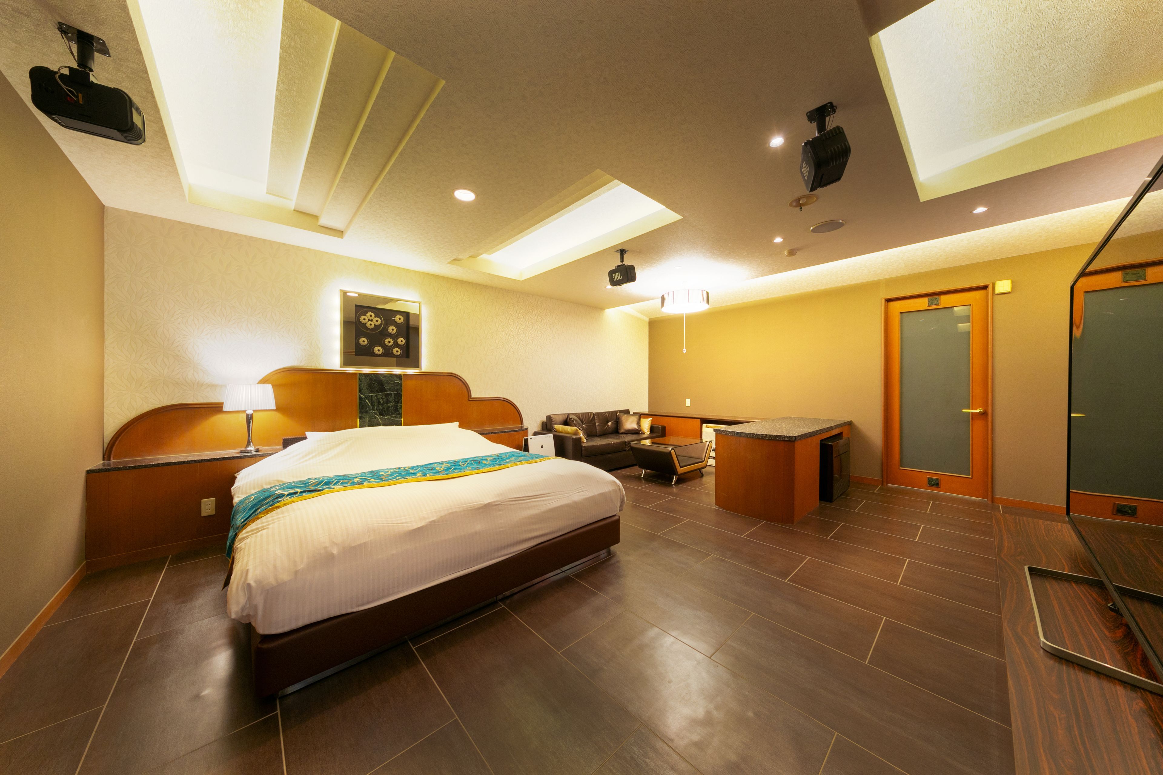 Une chambre d’hôtel avec un grand lit, un bureau, une chaise, un canapé, un miroir et un projecteur au plafond.