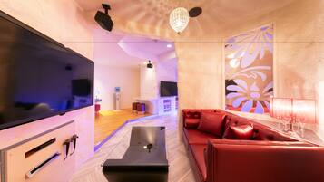 A modern living room with a flat-screen TV, a red leather sofa, a glass coffee table, and a decorative wall panel.