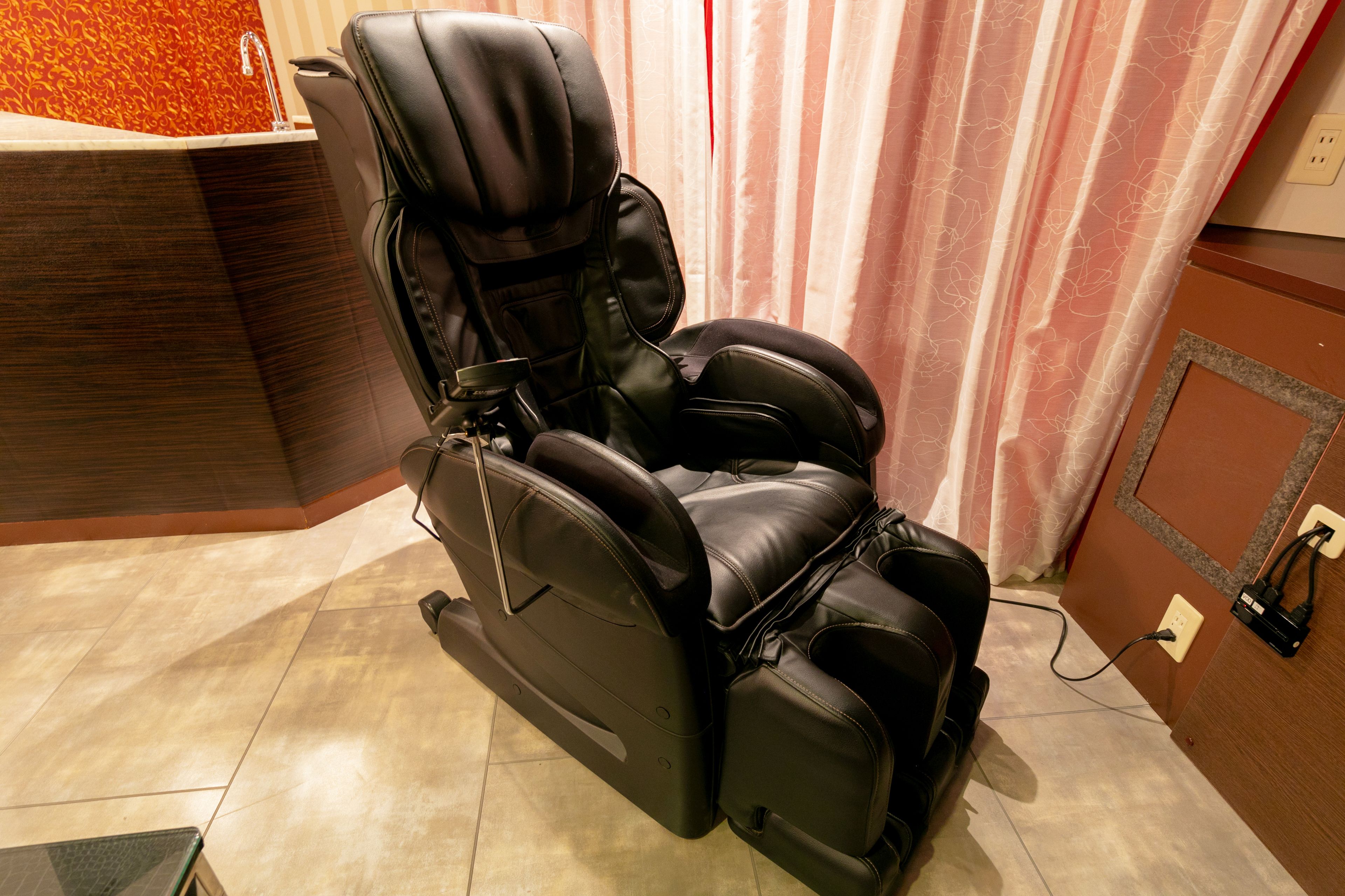 A massage chair in a room with a wooden floor and a curtain in the background.