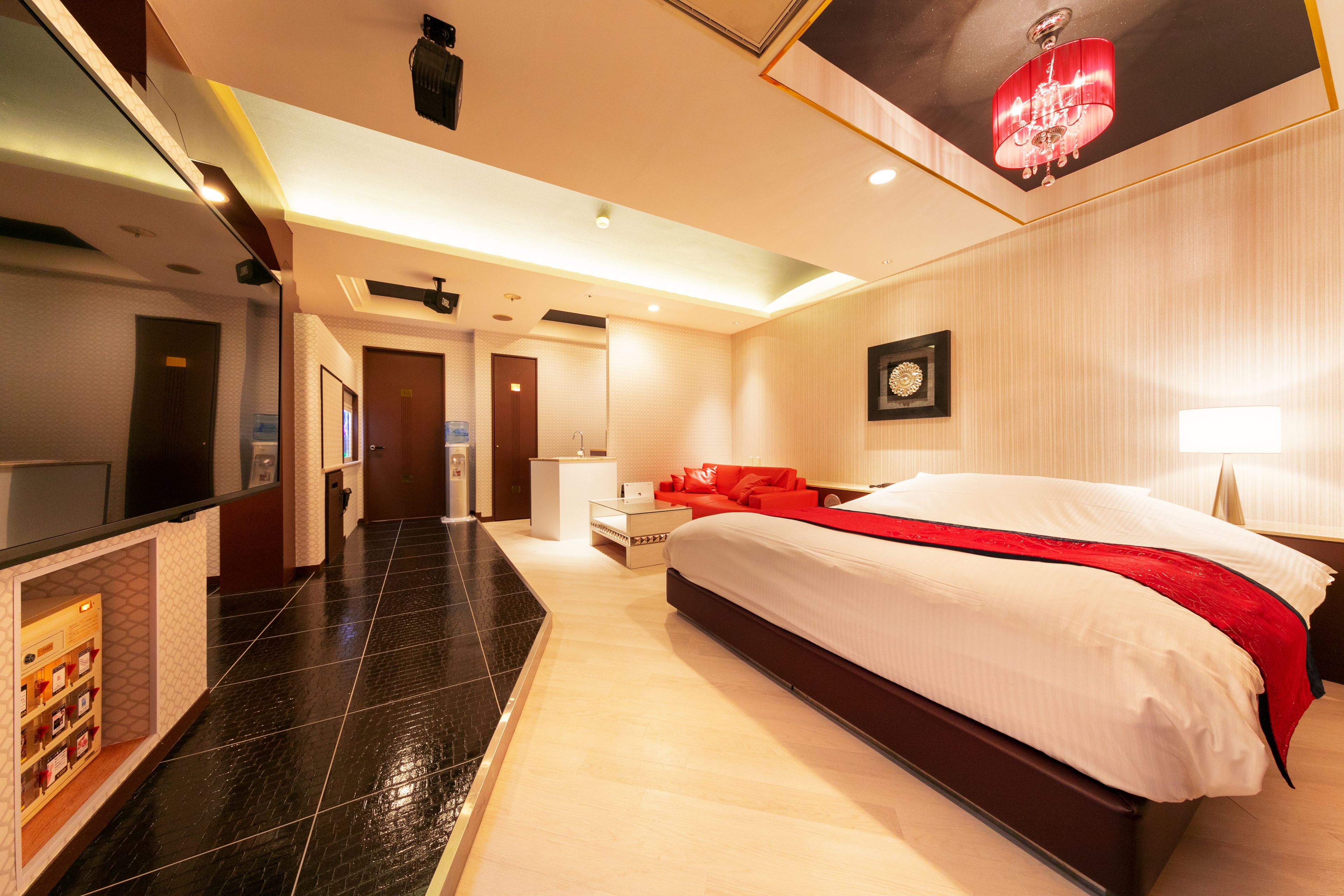 A hotel room with a large bed, a red accent wall, a TV, and a minibar.