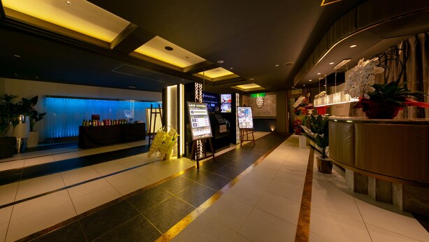 A hotel lobby with a reception desk, digital information boards, and a blue-lit wall.