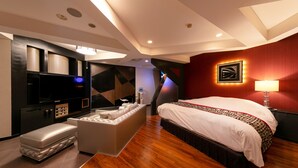 A modern hotel room with a large bed, a flat-screen TV, a seating area, and a minibar.