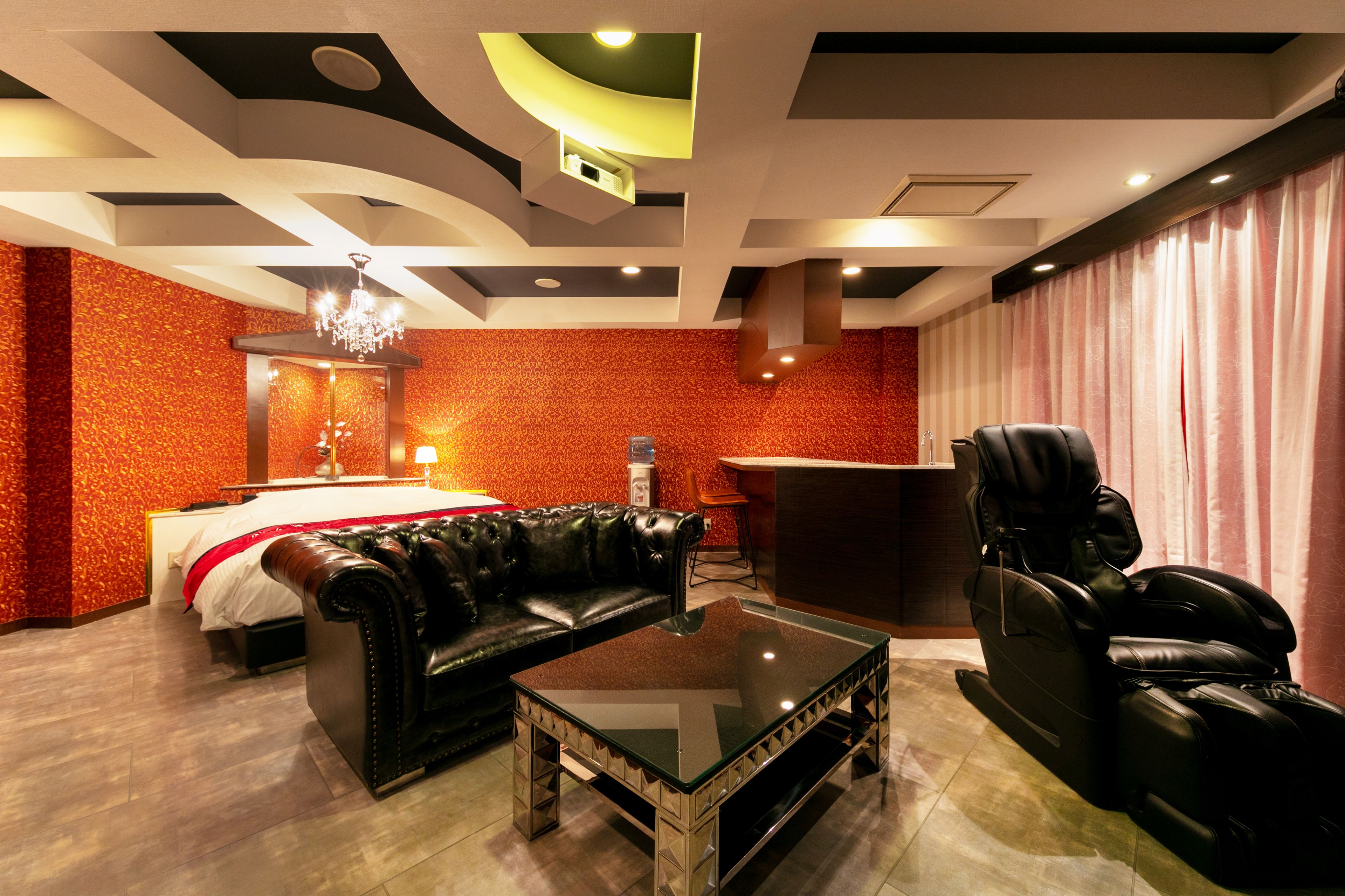 A hotel room with a bed, a leather sofa, a massage chair, and a glass coffee table.